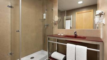 Un baño moderno con ducha de vidrio, tocador con encimera roja y espejo sobre el lavamanos.