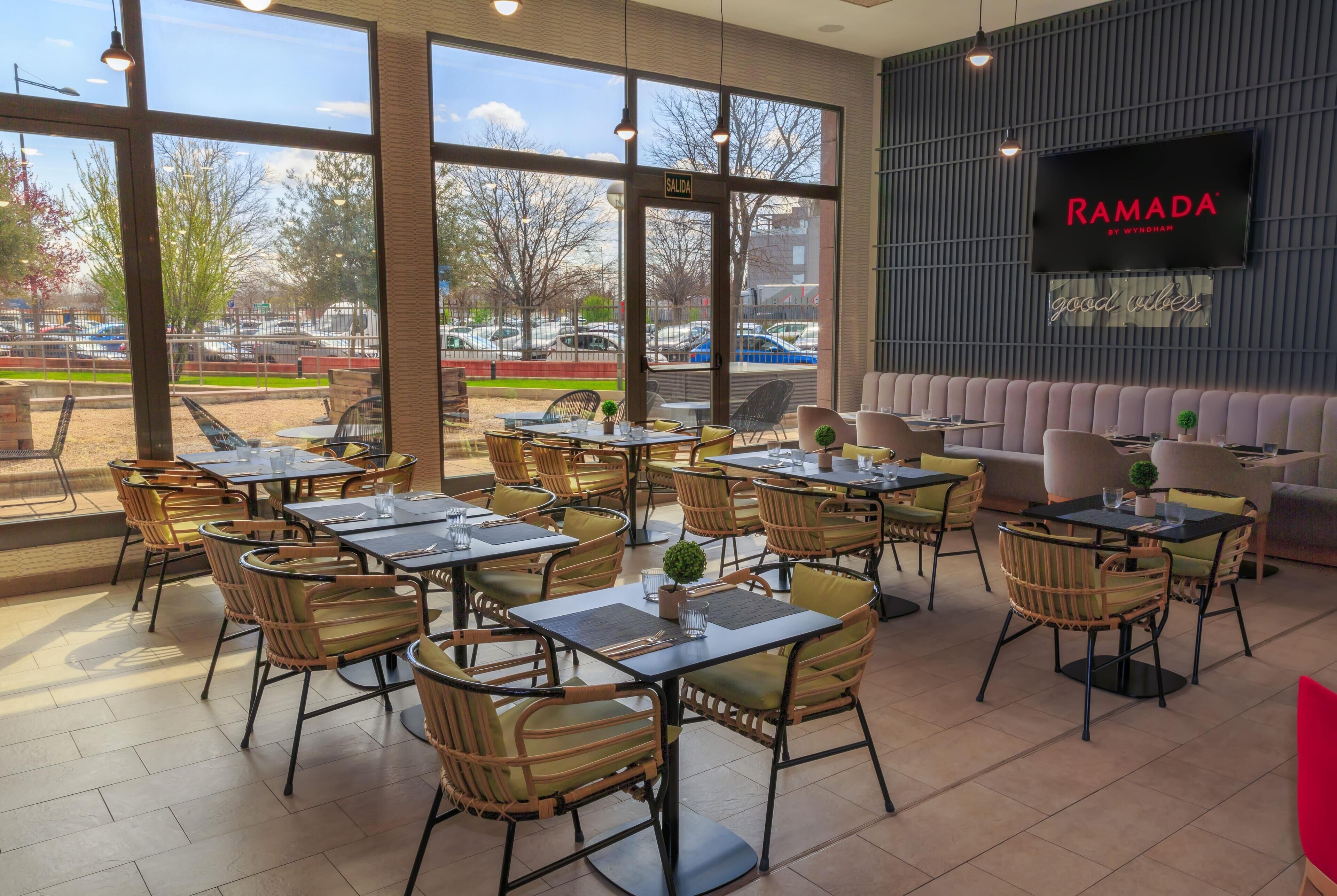 A restaurant with outdoor seating, large windows, and a TV screen displaying 'RAMADA BY WYNDHAM'.