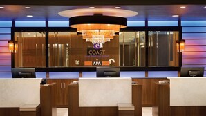 A hotel reception desk with a chandelier, wooden paneling, and a sign for the 'COAST' hotel by APA.