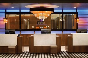 Ein Hotelrezeptionstresen mit einer Kandelaber, Holzvertäfelung und einem Schild für das Hotel 'COAST' von APA.