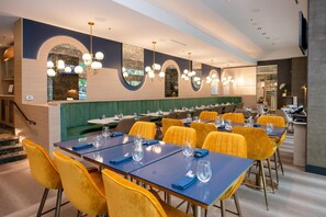 A restaurant with blue tables, yellow chairs, and a green booth area. - Coast Coal Harbour Vancouver Hotel by APA (Vancouver)