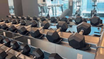 Eine Reihe hexagonaler Hanteln auf einem Gestell in einem Fitnessstudio mit großen Fenstern im Hintergrund.