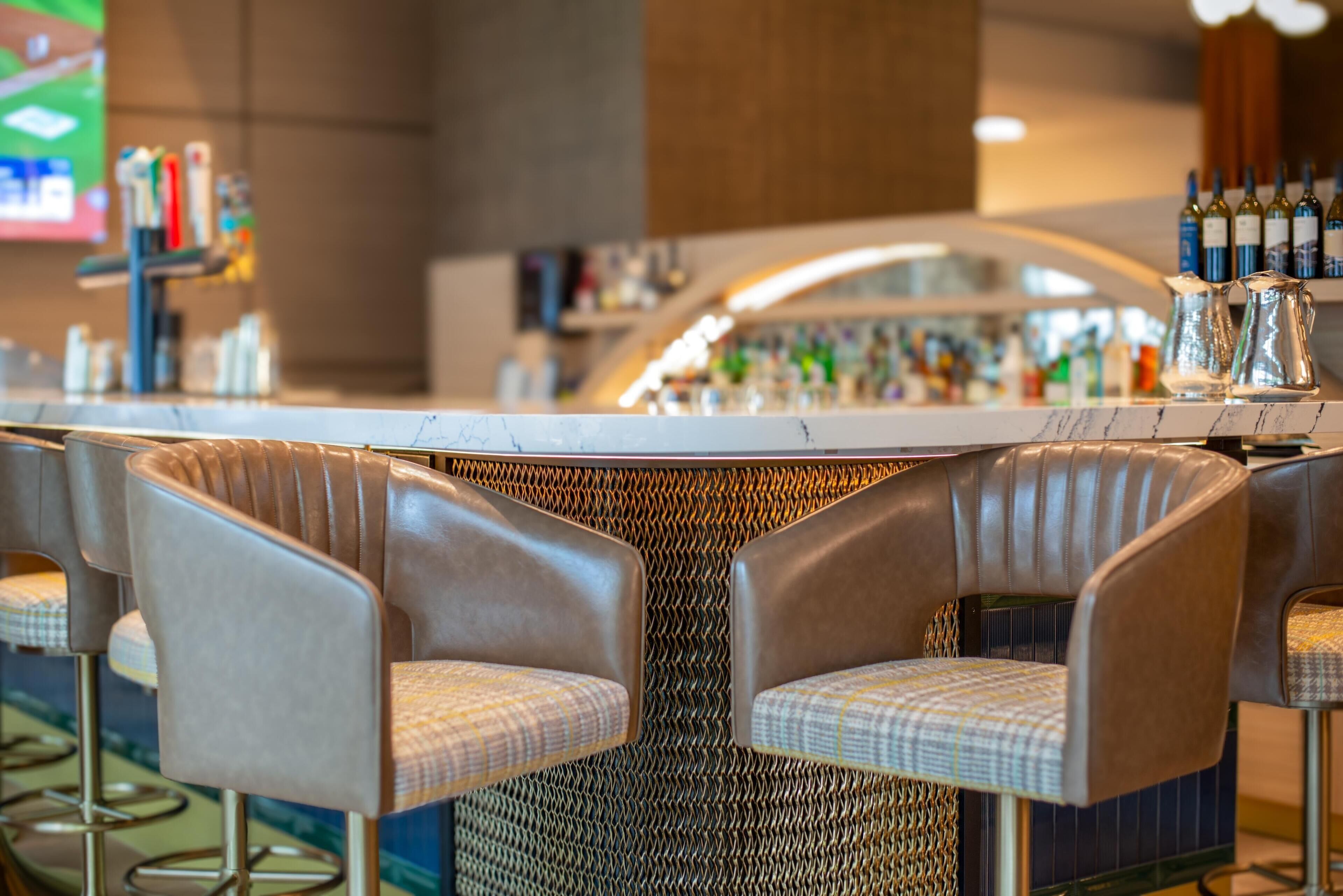 A bar area with a curved counter, two cushioned bar stools, and a variety of bottles on the shelves.