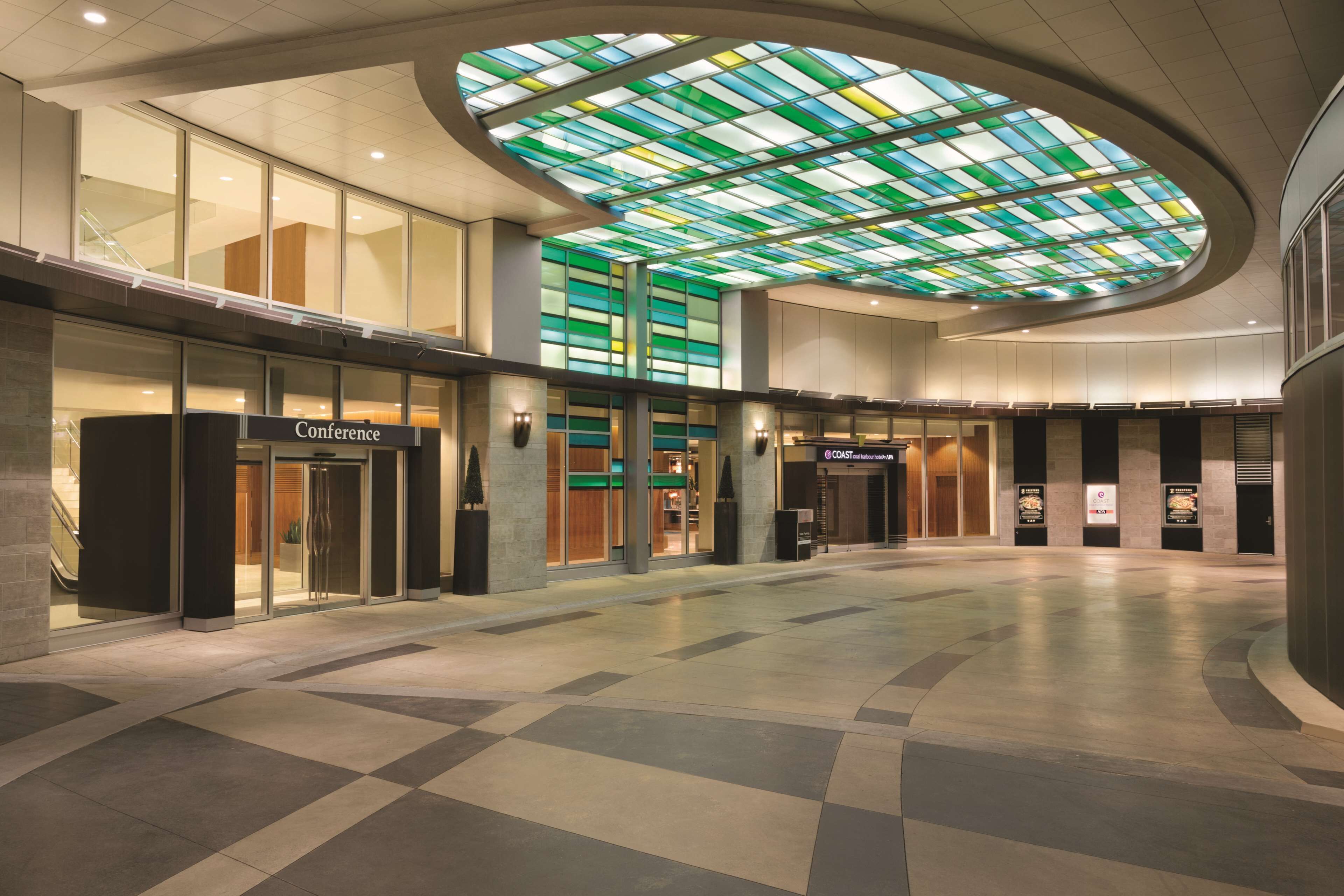 A spacious lobby with a large glass ceiling, a conference area, and a modern architectural design.