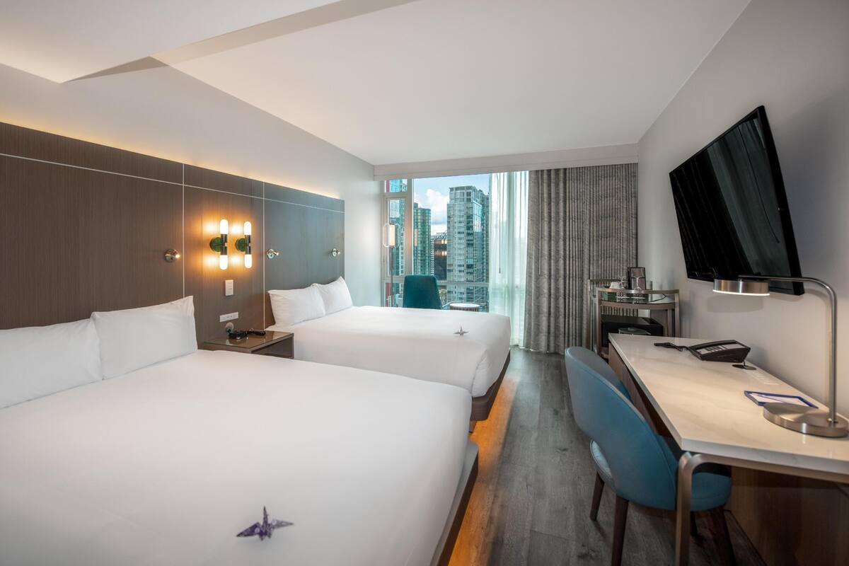 A hotel room with two beds, a desk, a chair, a TV, and a city view.