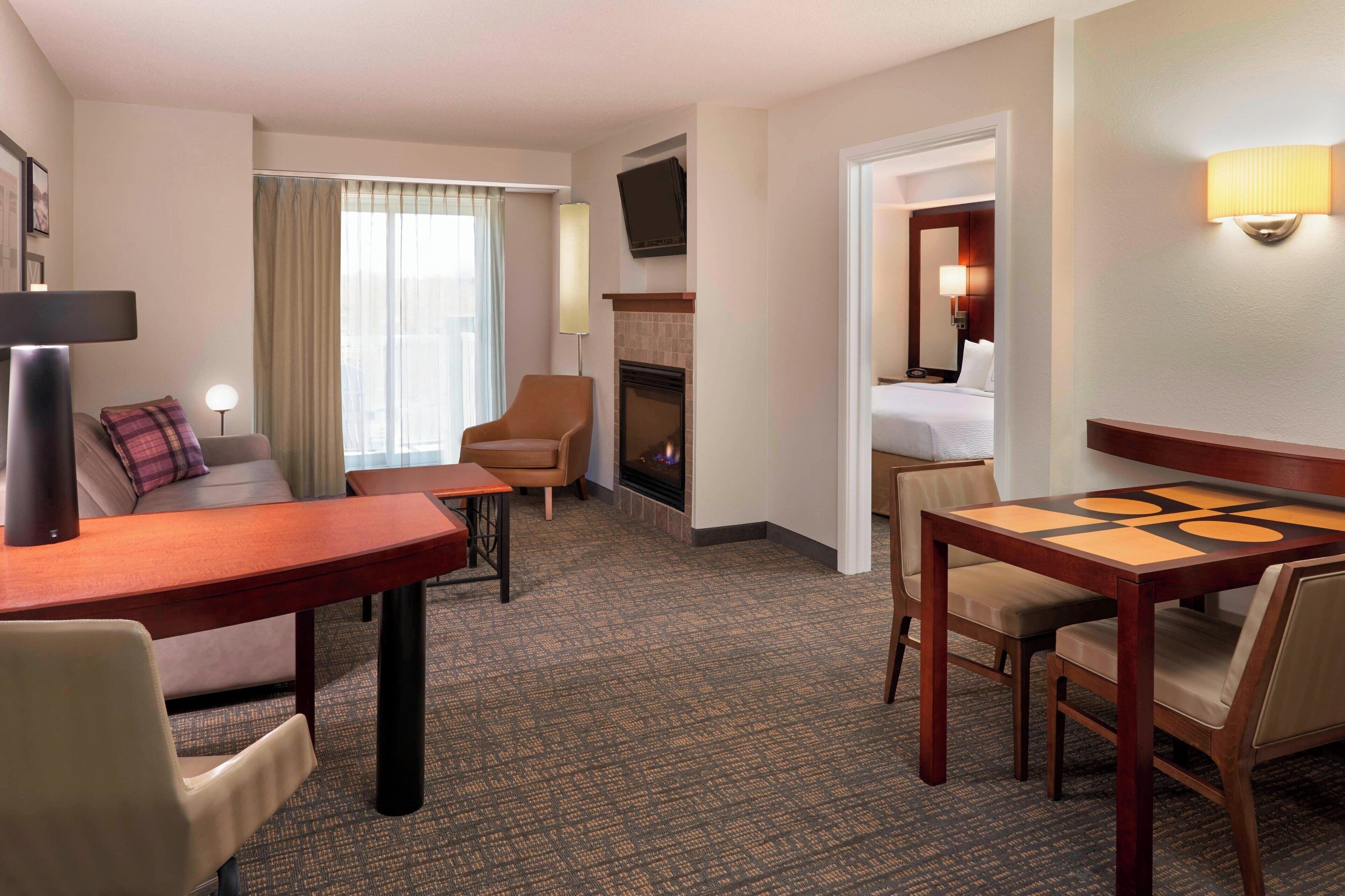 Une chambre d’hôtel avec un canapé, une petite table, une cheminée, un téléviseur fixé au mur et un lit.