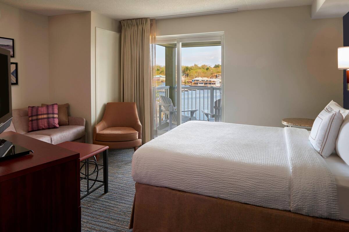 A hotel room with a large bed, a desk, a chair, and a balcony with a view of the water.