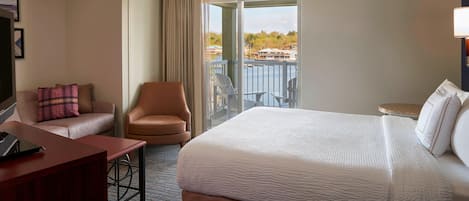 A hotel room with a large bed, a desk, a chair, and a balcony with a view of the water.