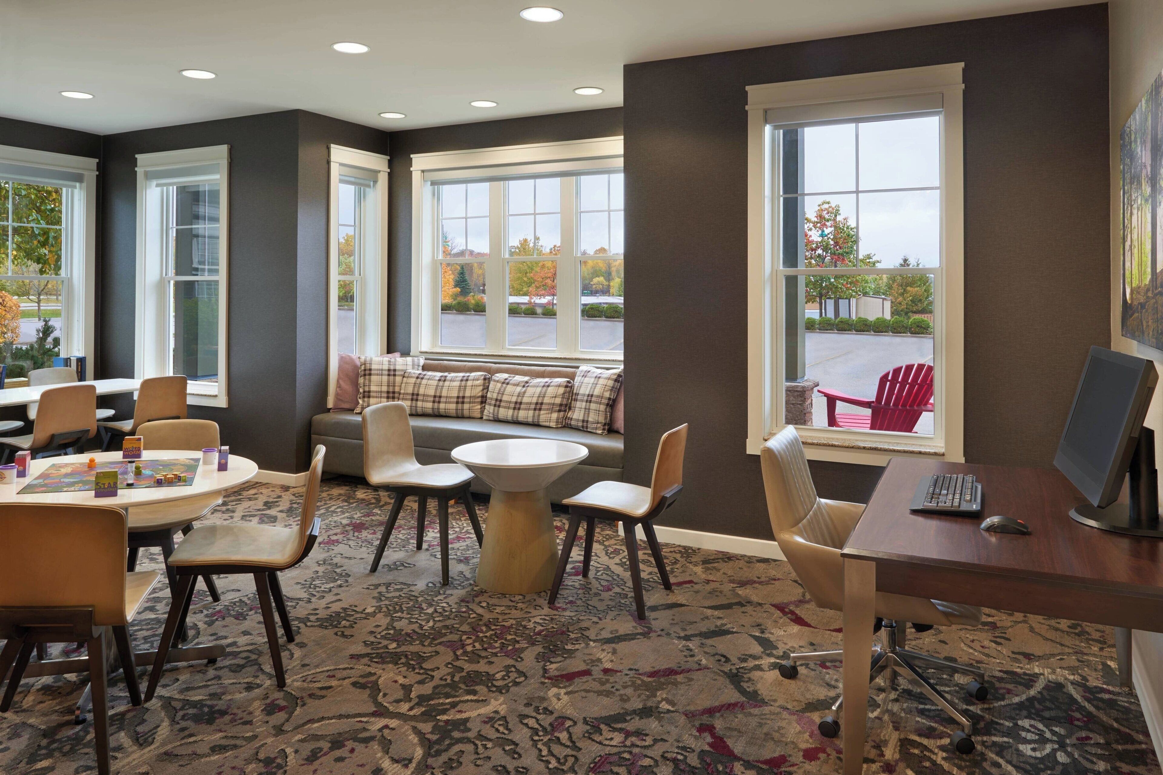 A modern room with a large window, a sofa, a round table, and a desk with a computer.