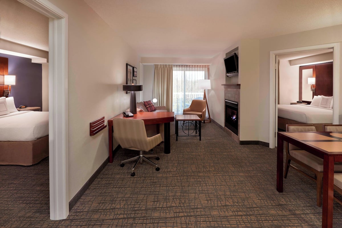 A hotel room with two beds, a desk, a chair, a TV, and a fireplace.