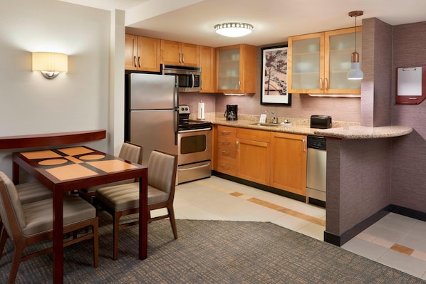 A compact kitchen with wooden cabinets, a refrigerator, microwave, oven, and a coffee maker. There is a dining table with chairs and a small rug. - Residence Inn by Marriott Gravenhurst Muskoka Wharf (Gravenhurst)