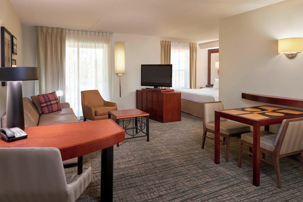 A hotel room with a sofa, armchair, small table, TV, and a bed.