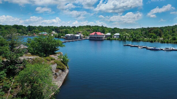 A lakeside property with docked boats, a red-roofed building, and lush greenery. - Residence Inn by Marriott Gravenhurst Muskoka Wharf (Gravenhurst)