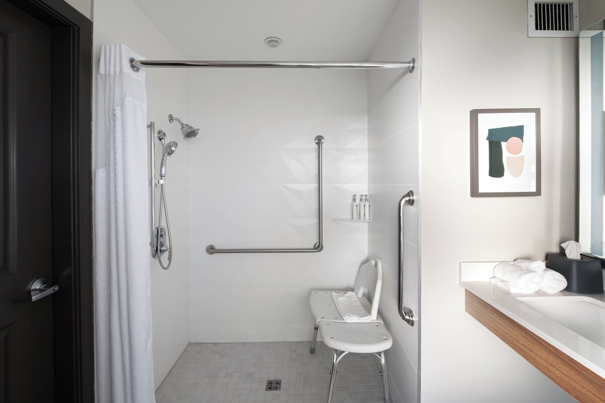 A modern bathroom with a shower, a toilet, a bench, and a sink with a towel rack.