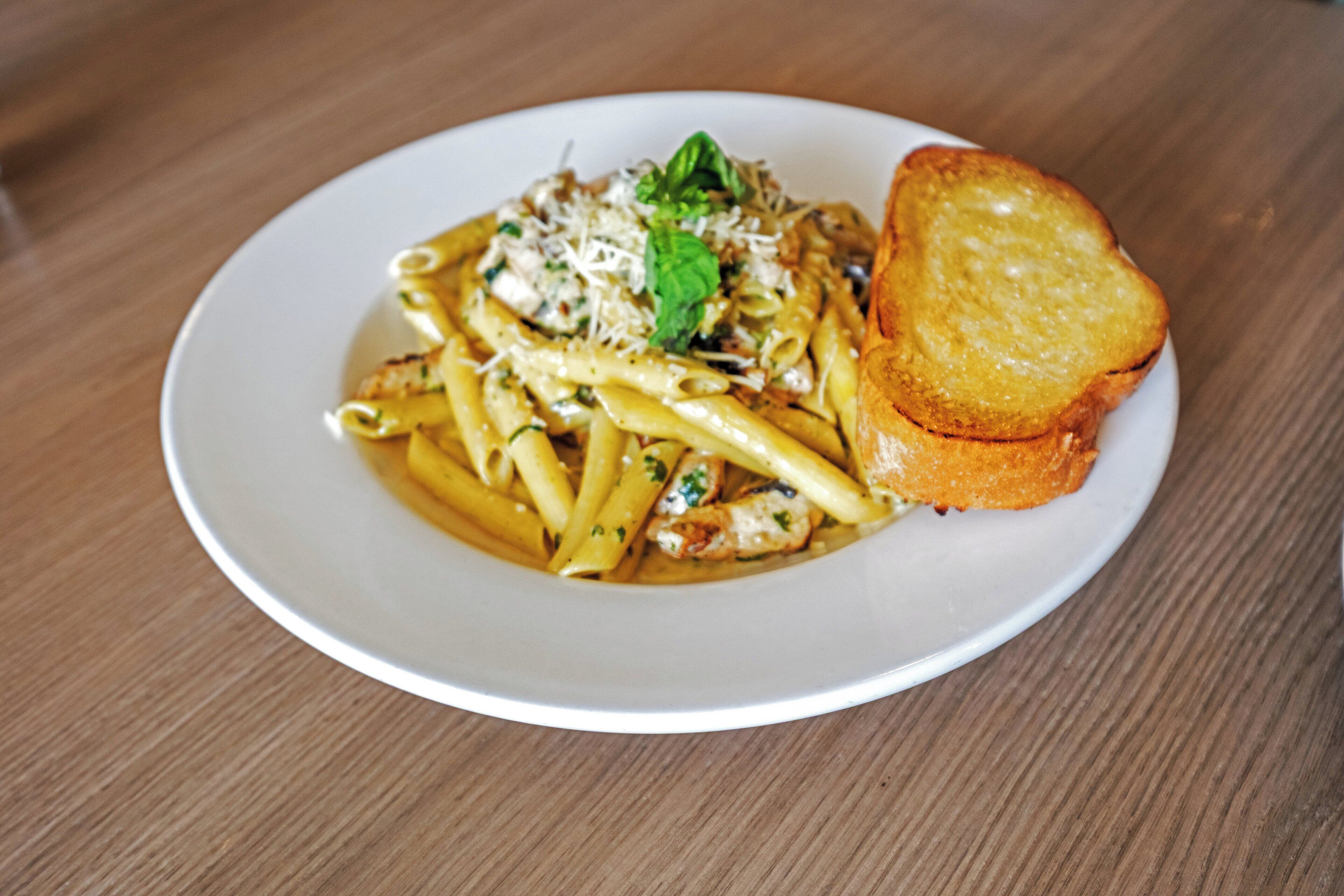 Un plato de pasta con una rebanada de pan tostado sobre un plato blanco.
