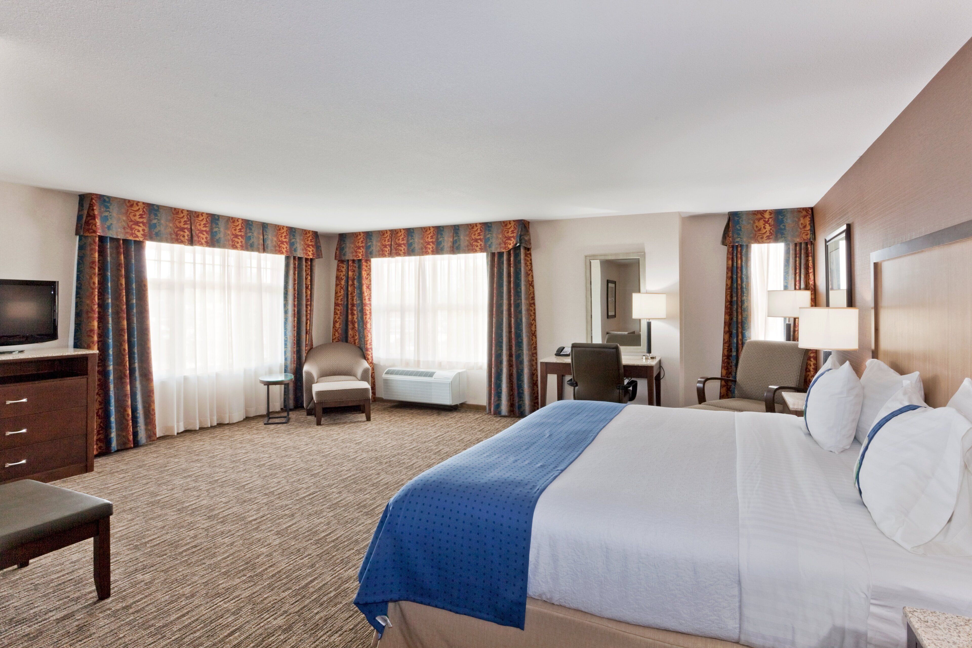 A hotel room with a large bed, a desk, a chair, a television, and a window with curtains.