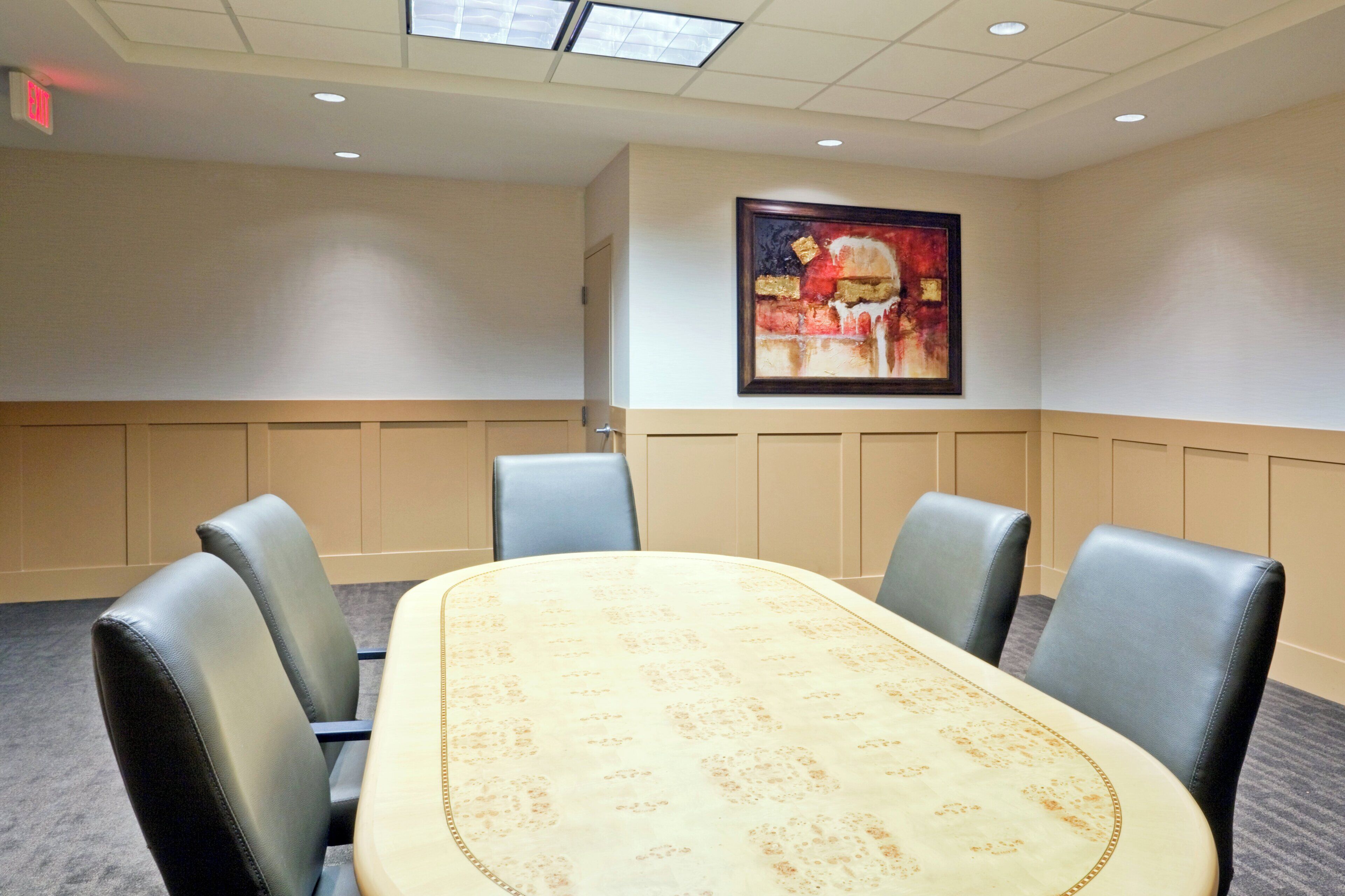 A conference room with a large oval table, four chairs, and a painting on the wall.