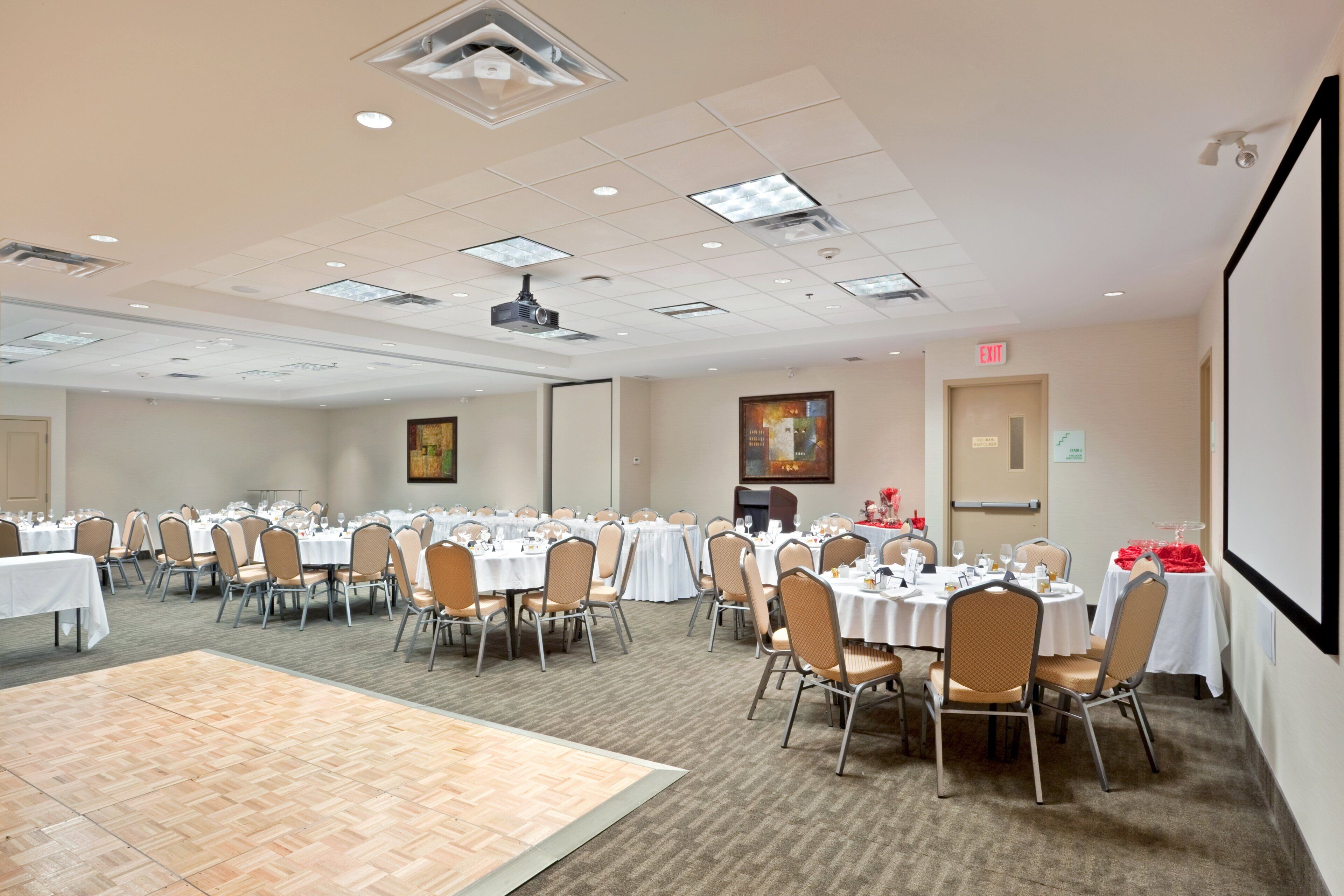 A conference room with multiple tables and chairs, a projector, and a screen on the wall.
