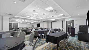 A conference room with multiple tables and chairs, a projector screen, and a presentation area.
