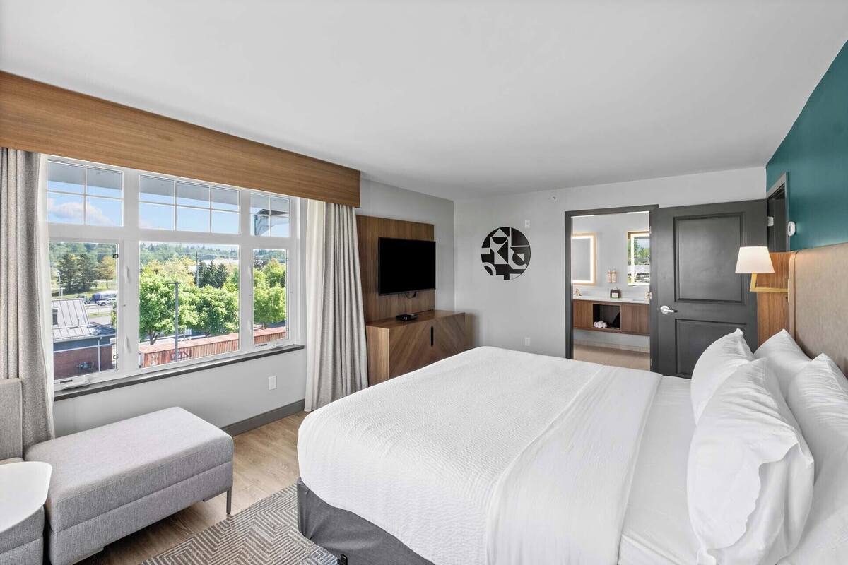 A hotel room with a large bed, a TV, a desk, and a bathroom visible through an open door.