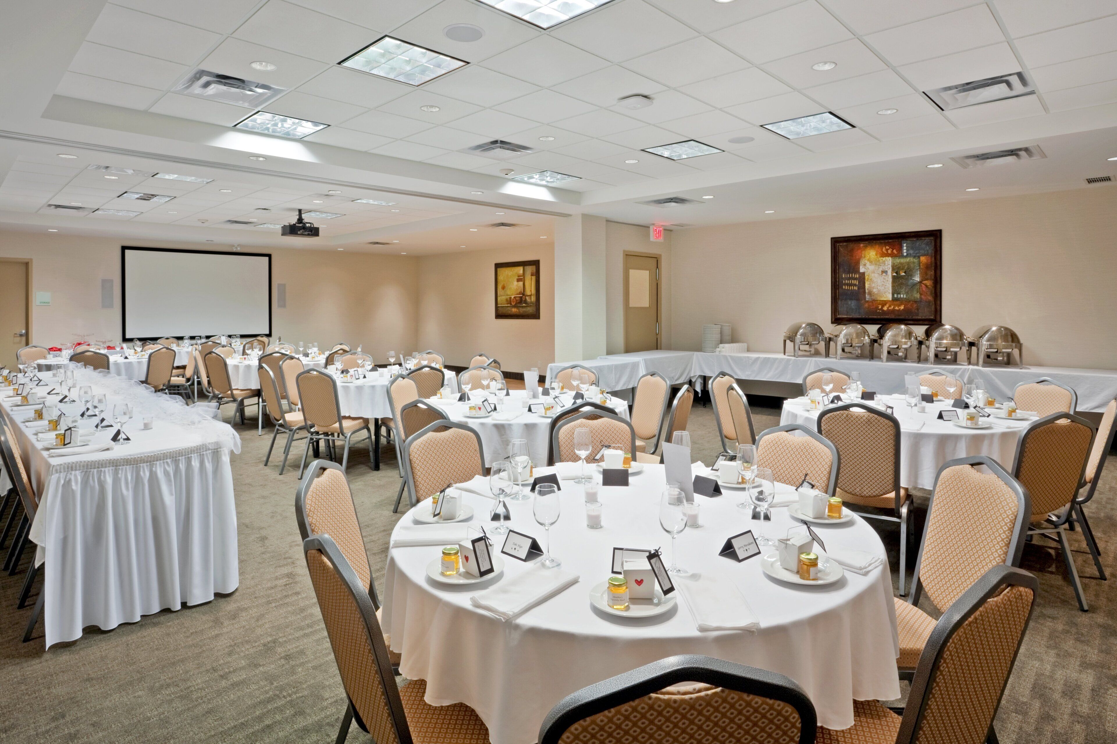 A conference room with multiple round tables, each set with white tablecloths, chairs, and various dining items.