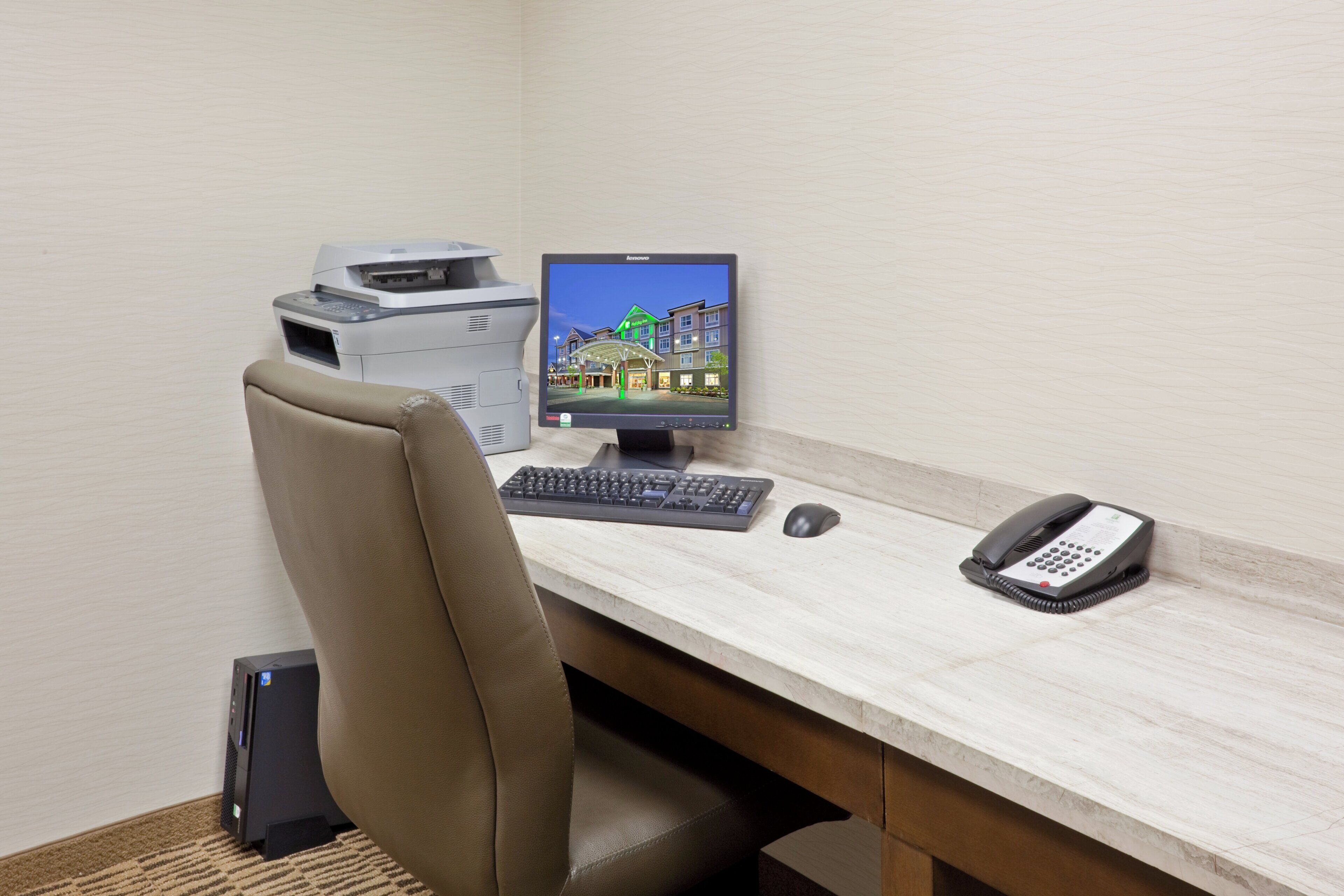 A hotel office desk with a computer, keyboard, mouse, and telephone.