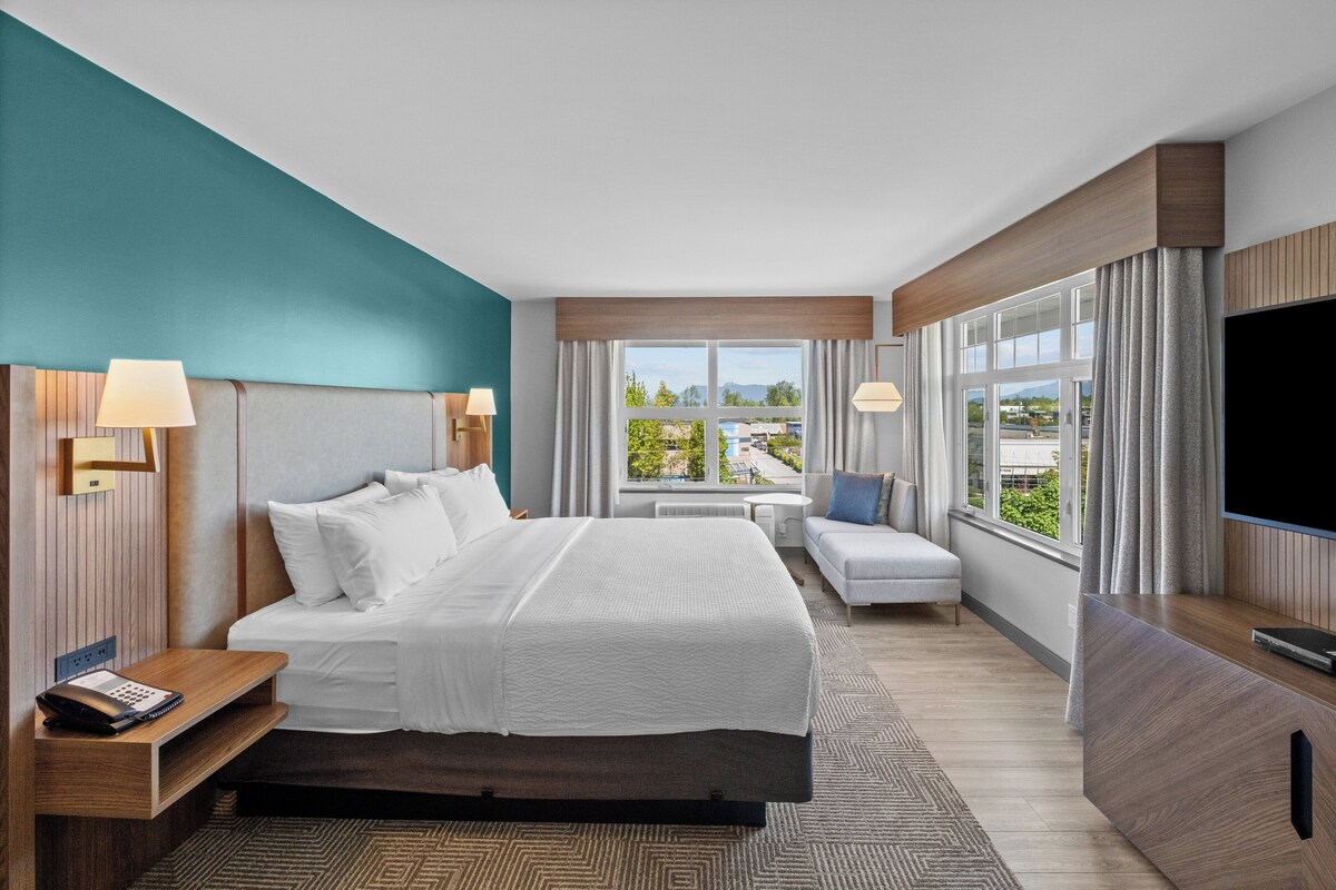 Une chambre d’hôtel moderne dotée d’un grand lit, d’un bureau, d’une télévision à écran plat et offrant une vue sur l’extérieur.
