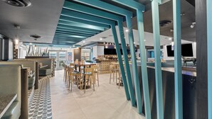 Un restaurante moderno con techos altos, vigas estructurales color turquesa y piso estampado.