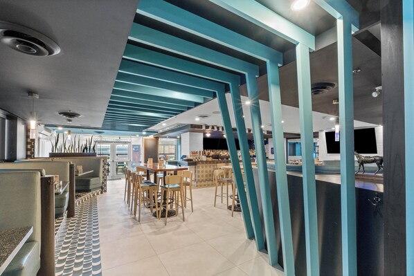 Een modern restaurant met hoge plafonds, blauwgroene structurele balken en een patroon vloer.
