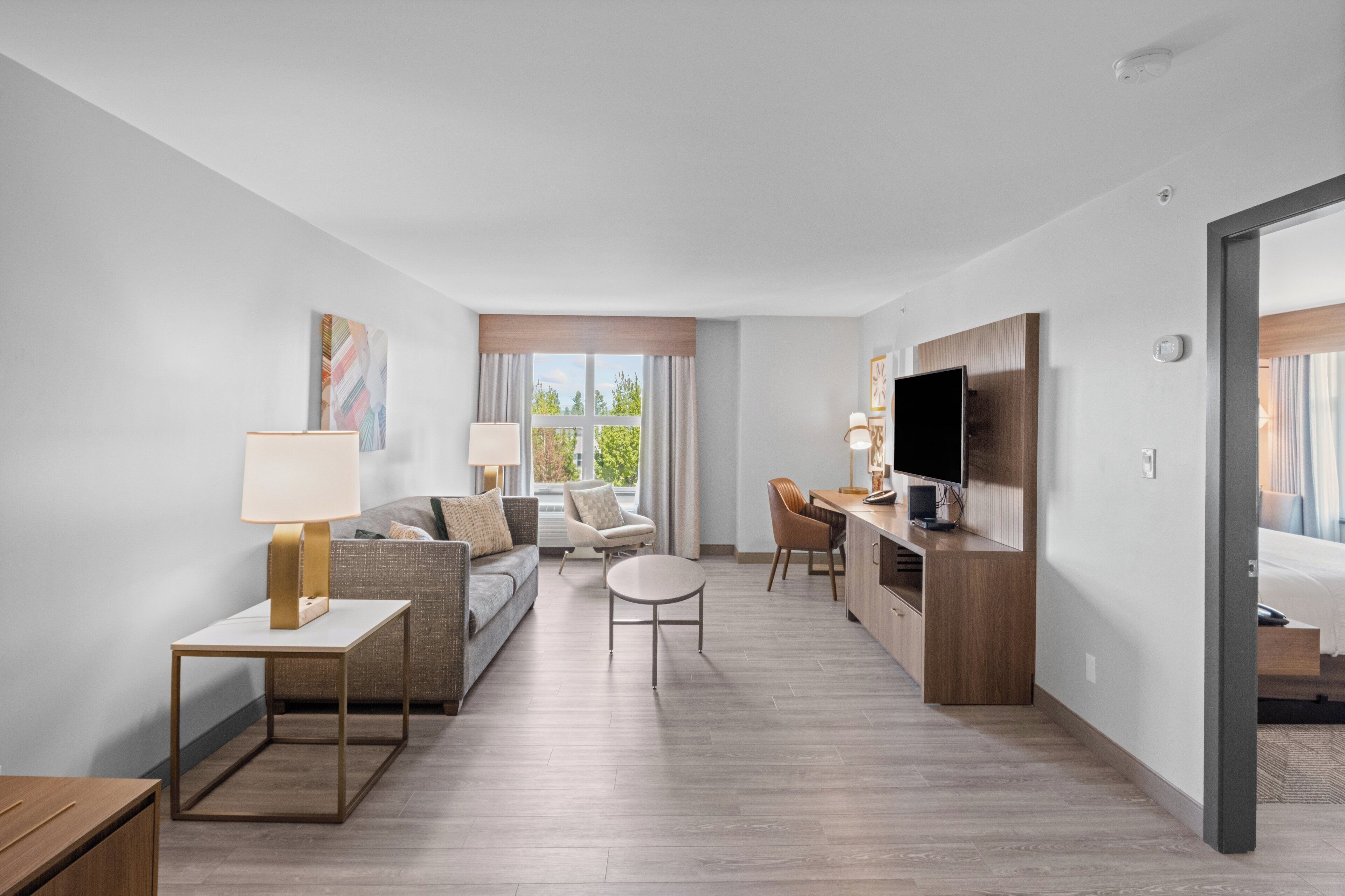 A modern hotel room with a sofa, a dining table, a TV, and a small desk.