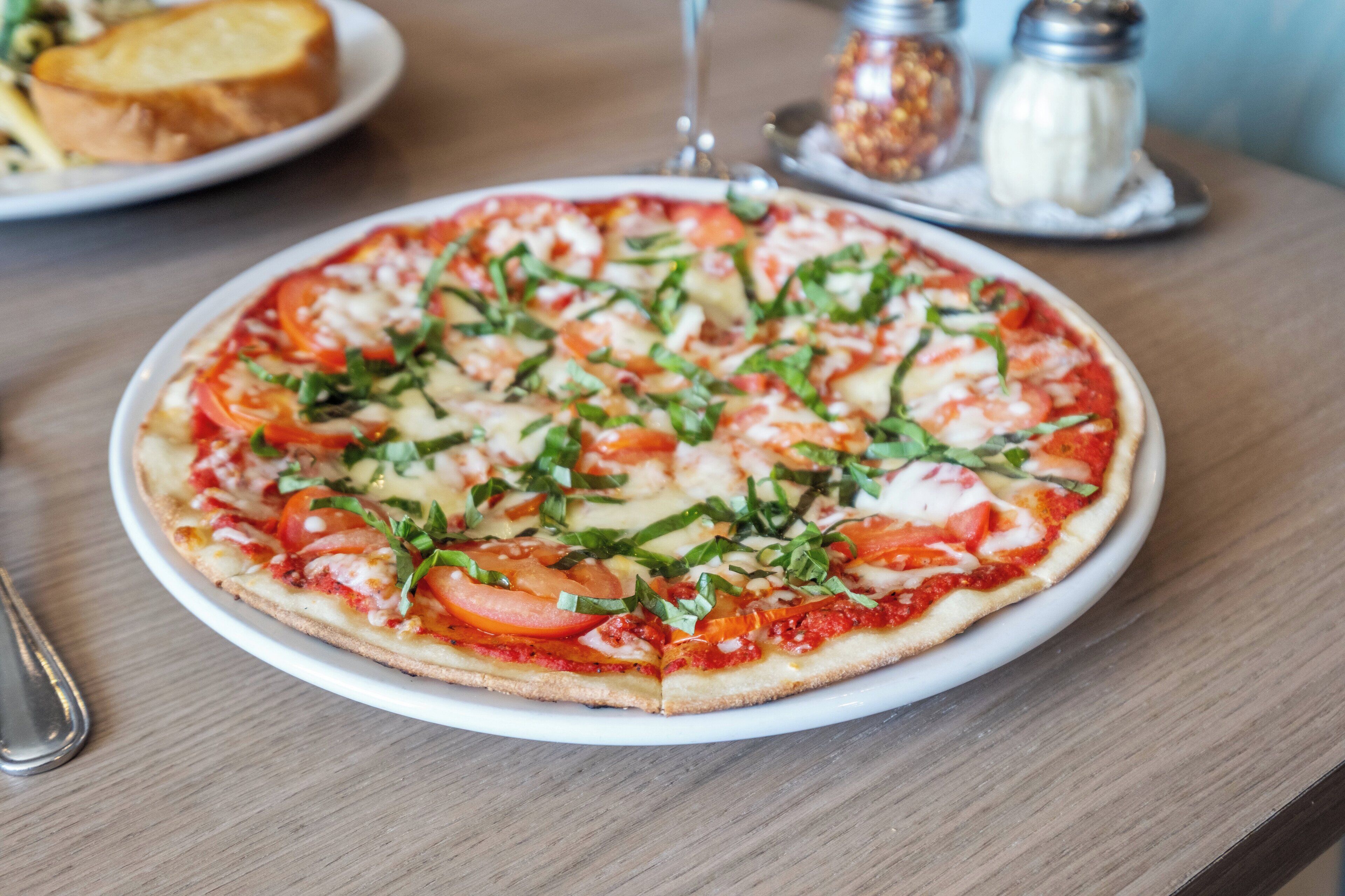 Pizza met tomaten en basilicum op een wit bord.