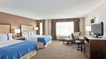 A hotel room with two beds, a desk, a chair, a television, and an air conditioning unit.