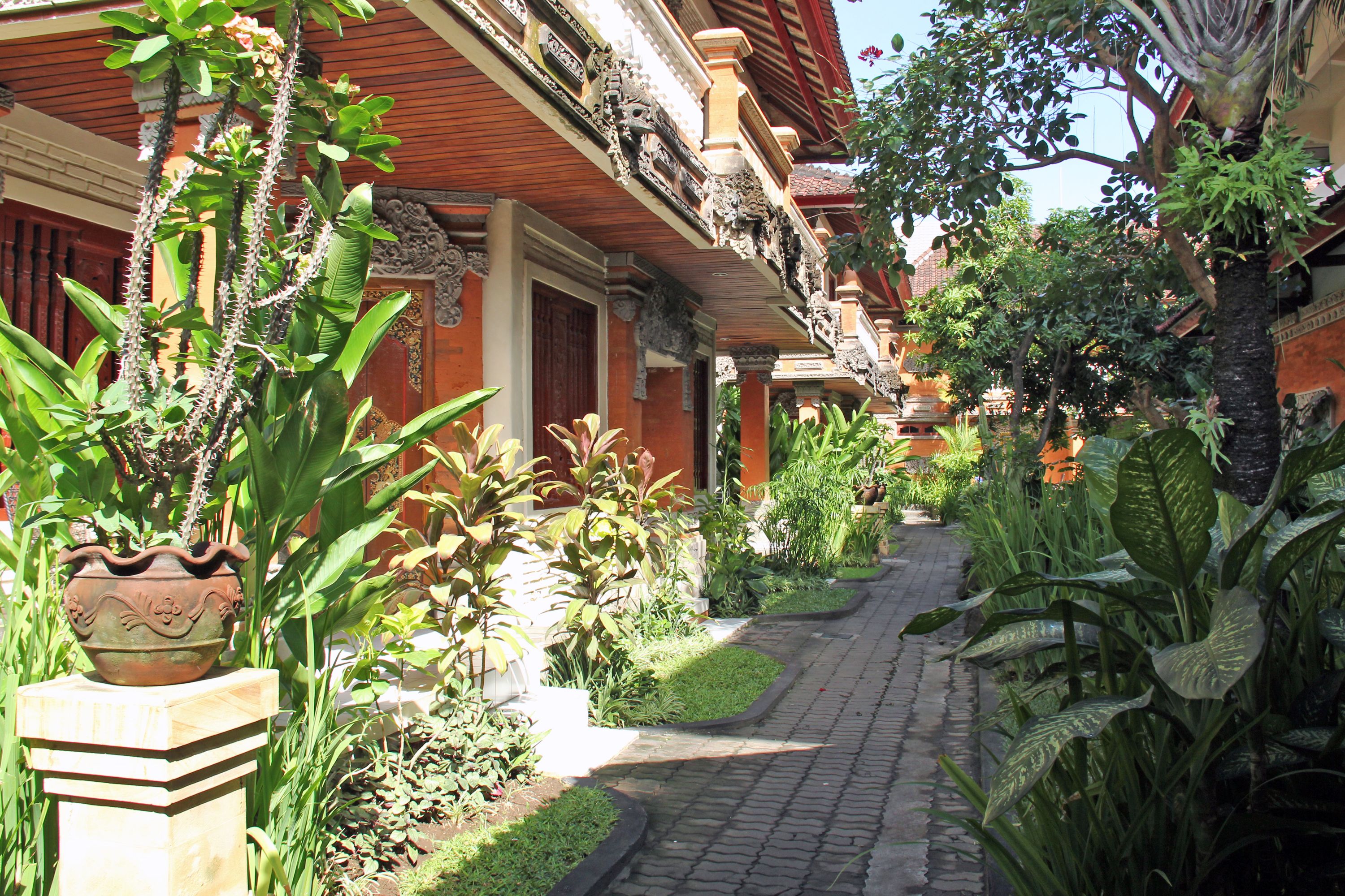 A traditional courtyard with a cobblestone pathway, surrounded by lush greenery and ornate architectural details.