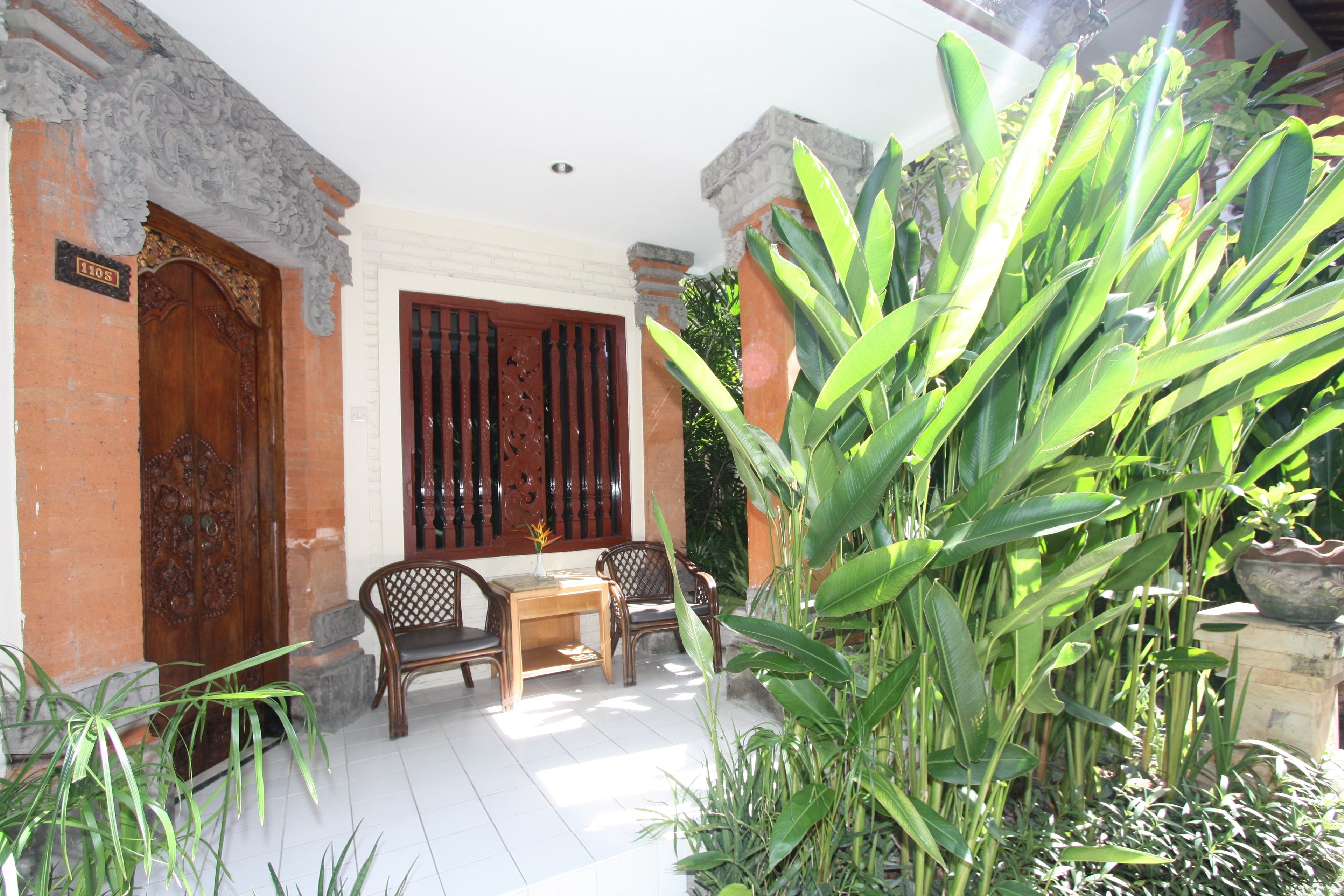 A traditional wooden door with a sign above it, a wooden bench, a table, and a potted plant in the foreground.