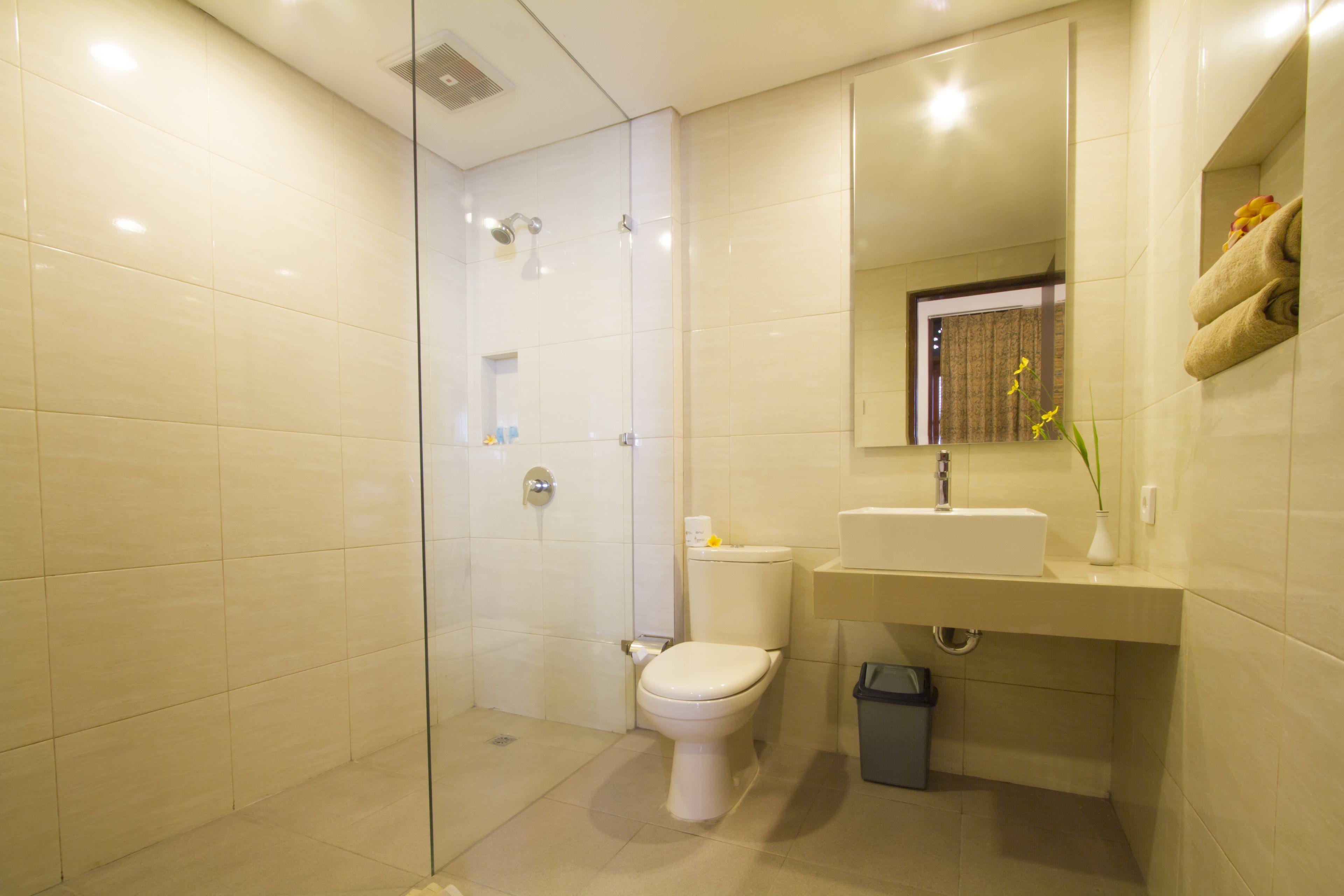 Un baño moderno con ducha envuelta en vidrio, inodoro blanco y lavamanos con espejo superior.