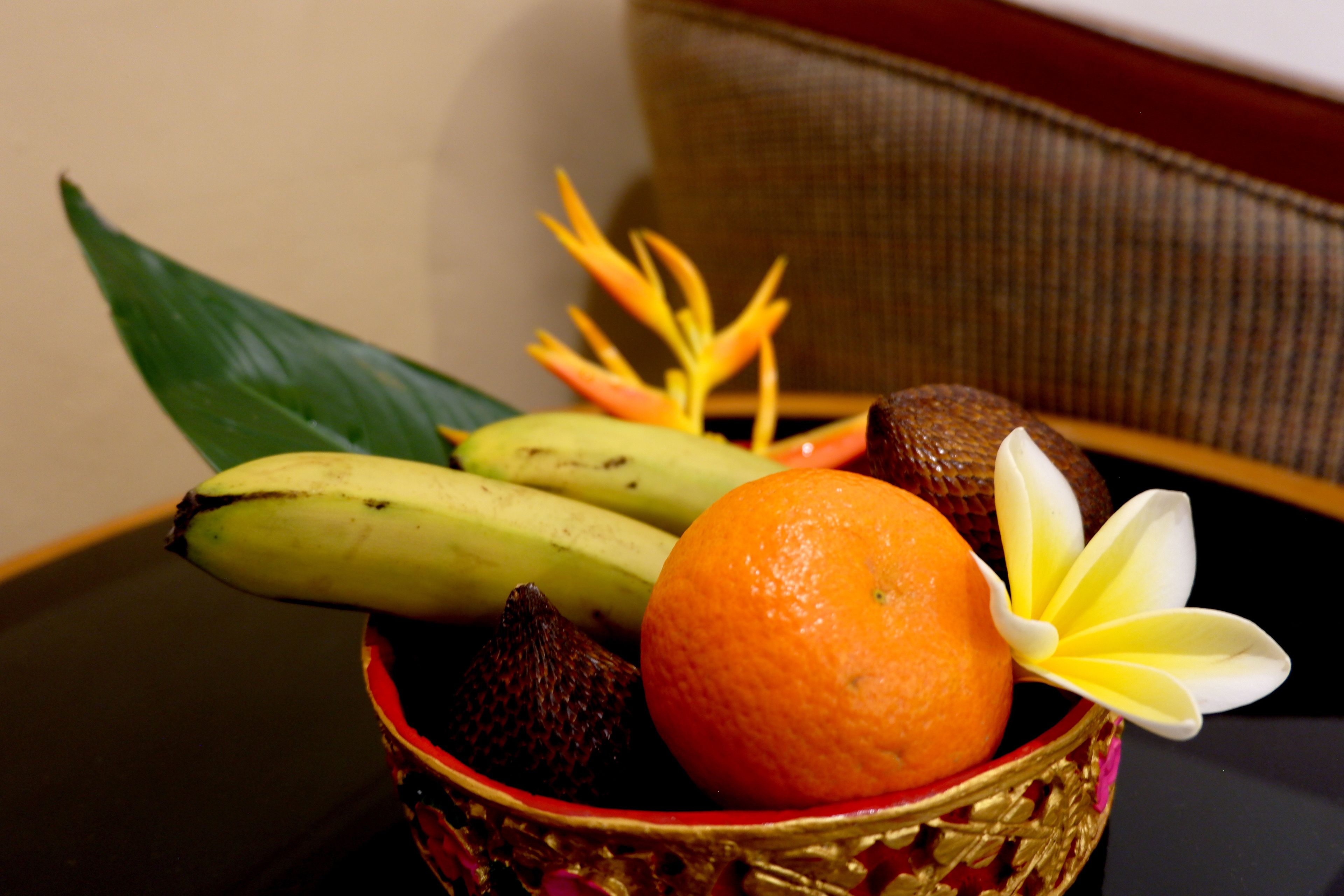 A bowl containing bananas, an orange, and a flower.