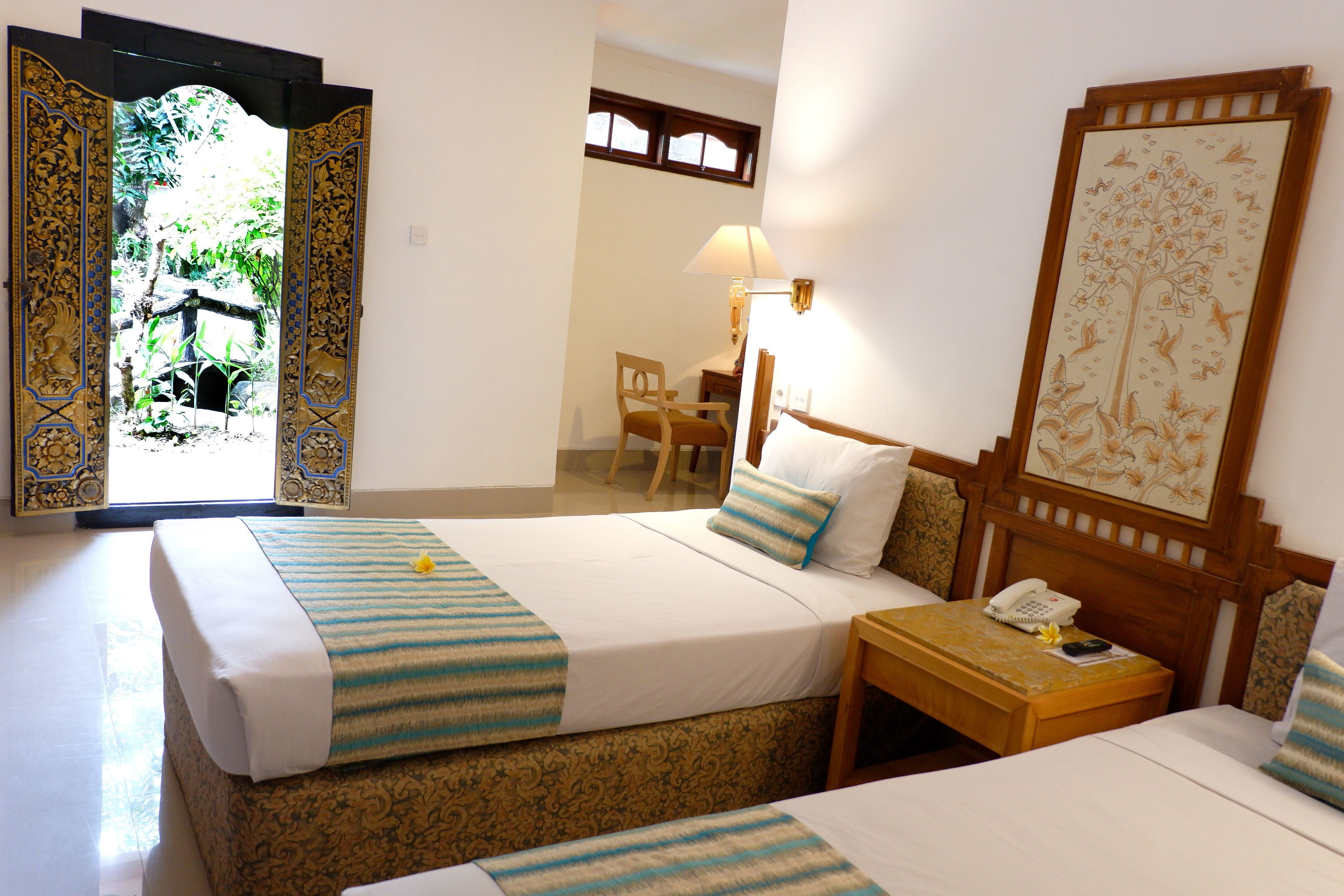 Quarto de hotel com duas camas, uma escrivaninha, uma cadeira, um abajur e um telefone.