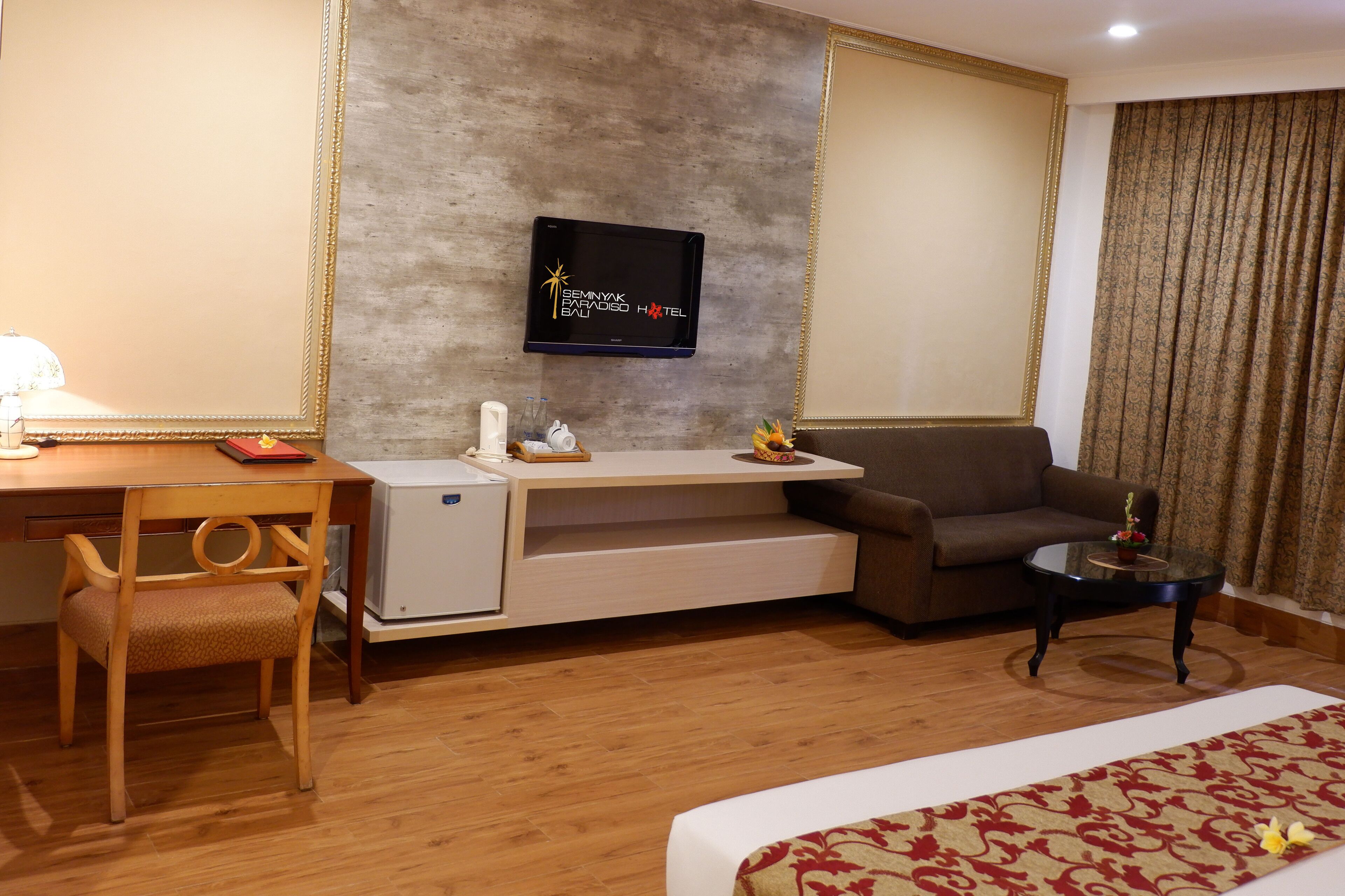 A hotel room with a wooden desk, a sofa, a small table, a bed, and a TV mounted on the wall.