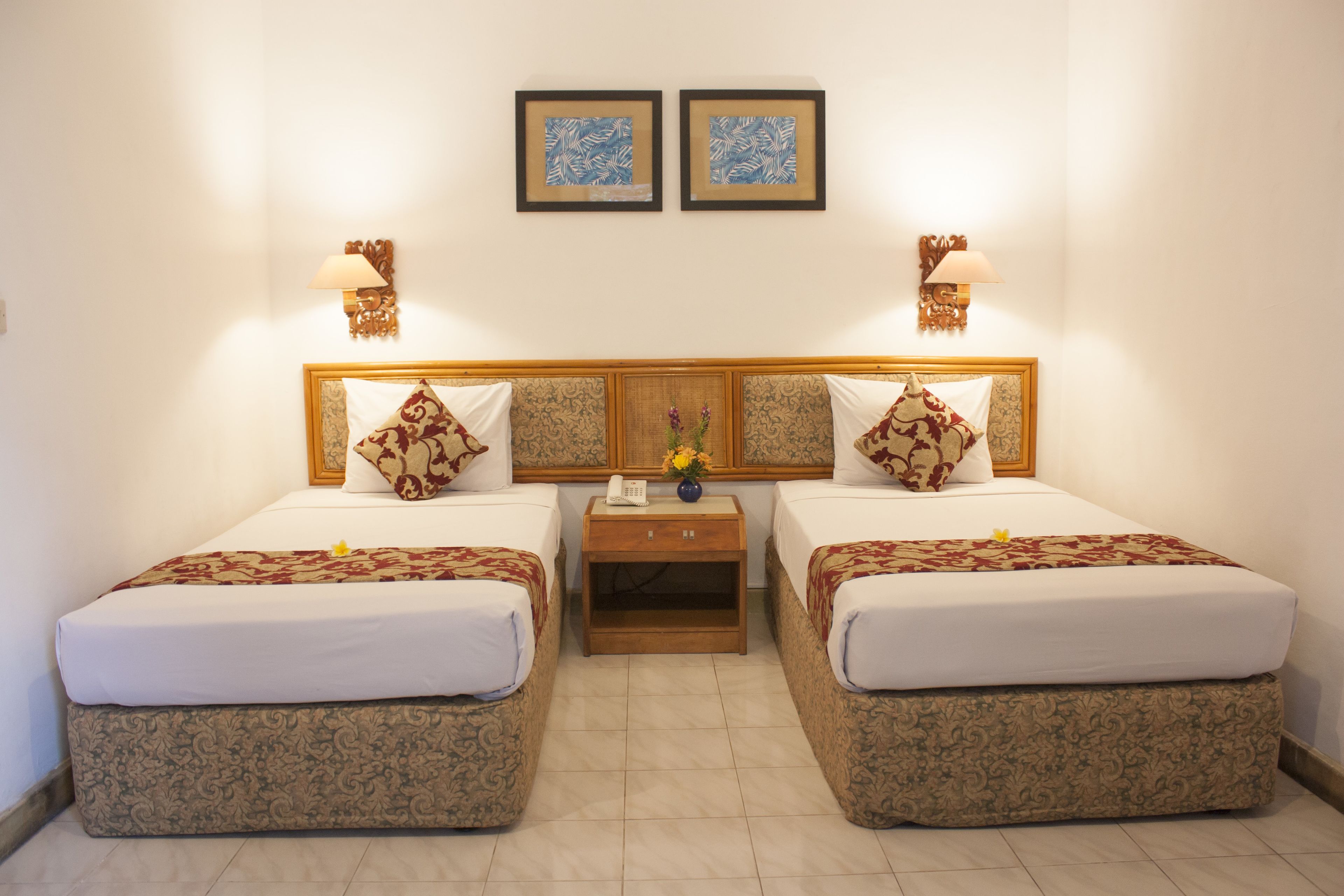 Una habitación de hotel con dos camas, una mesita de noche y dos lámparas fijadas a la pared.