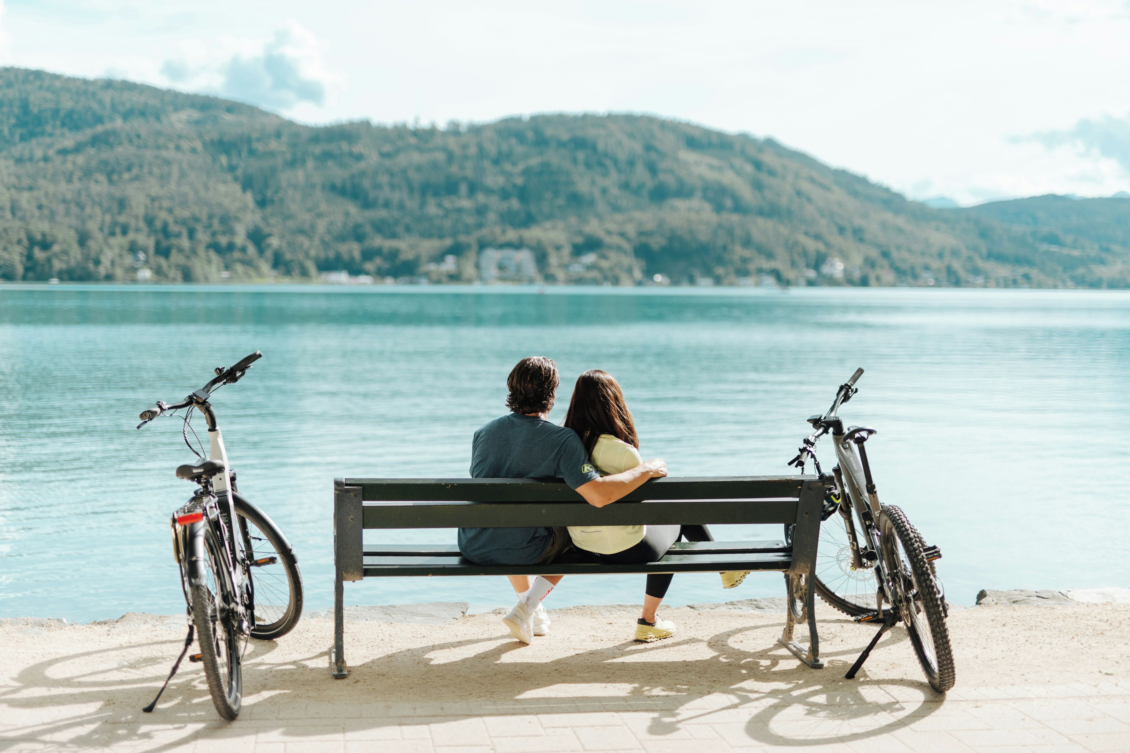 A couple sitting on a bench by a lake with bicycles parked nearby.