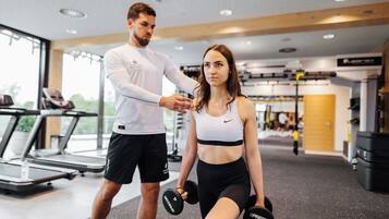A gym with exercise equipment, a treadmill, and a person holding dumbbells.