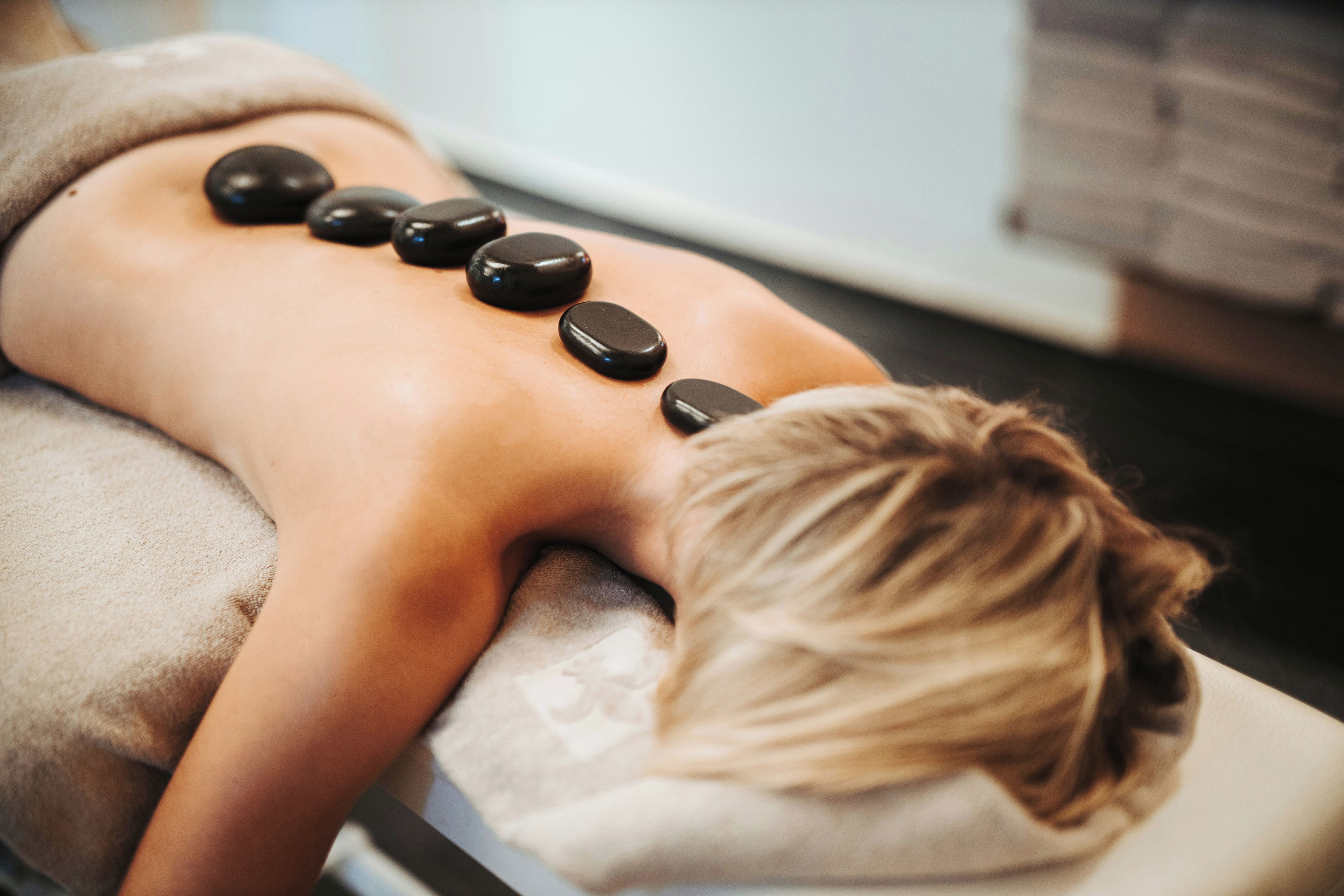Eine Person liegt auf einer Massageliege, auf deren Rücken mehrere schwarze Steine liegen.
