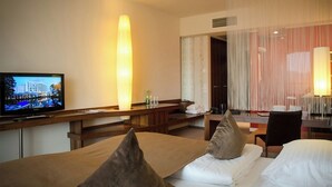 A hotel room with a bed, a desk with a television, and a large window with curtains. - Seepark Wörthersee Resort (Klagenfurt am Woerthersee)