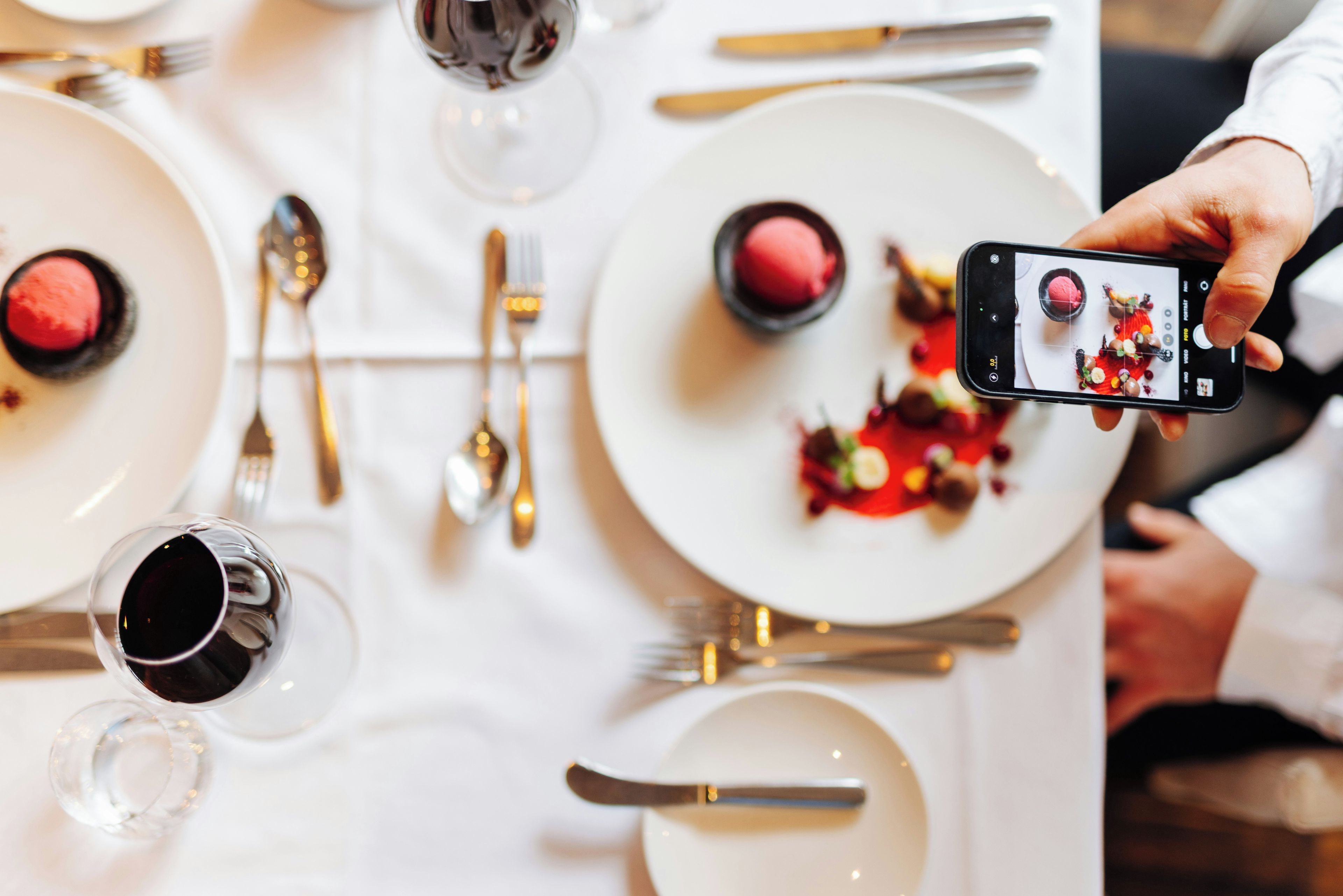 A dining table with plates of food, cutlery, and a smartphone being used to take a photo.