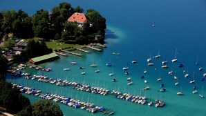 An aerial view of a marina with numerous boats docked, surrounded by lush greenery and a few buildings. - Seepark Wörthersee Resort (Klagenfurt am Woerthersee)