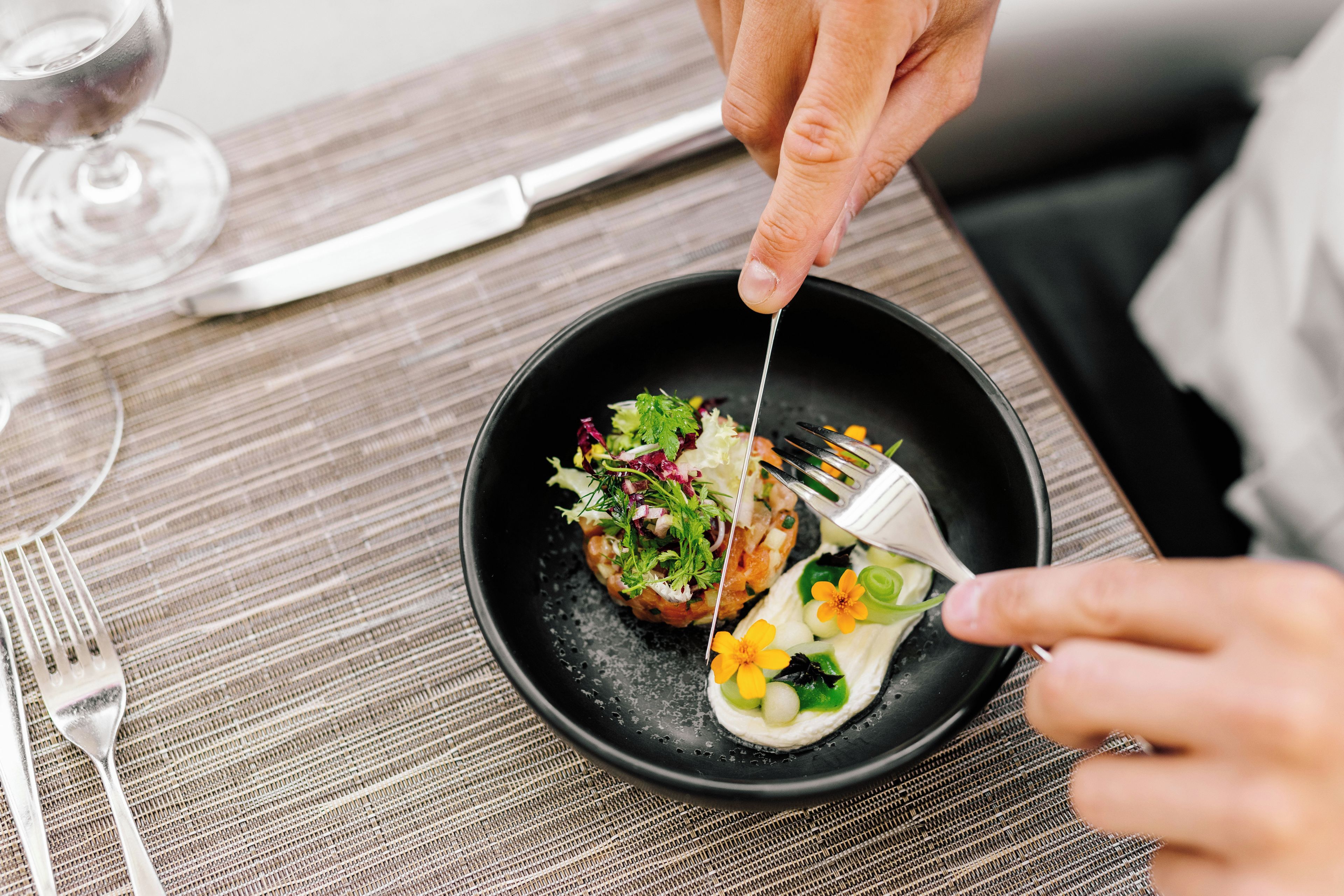 Una persona usando un tenedor para comer un plato sobre un mantel individual tejido en una mesa.