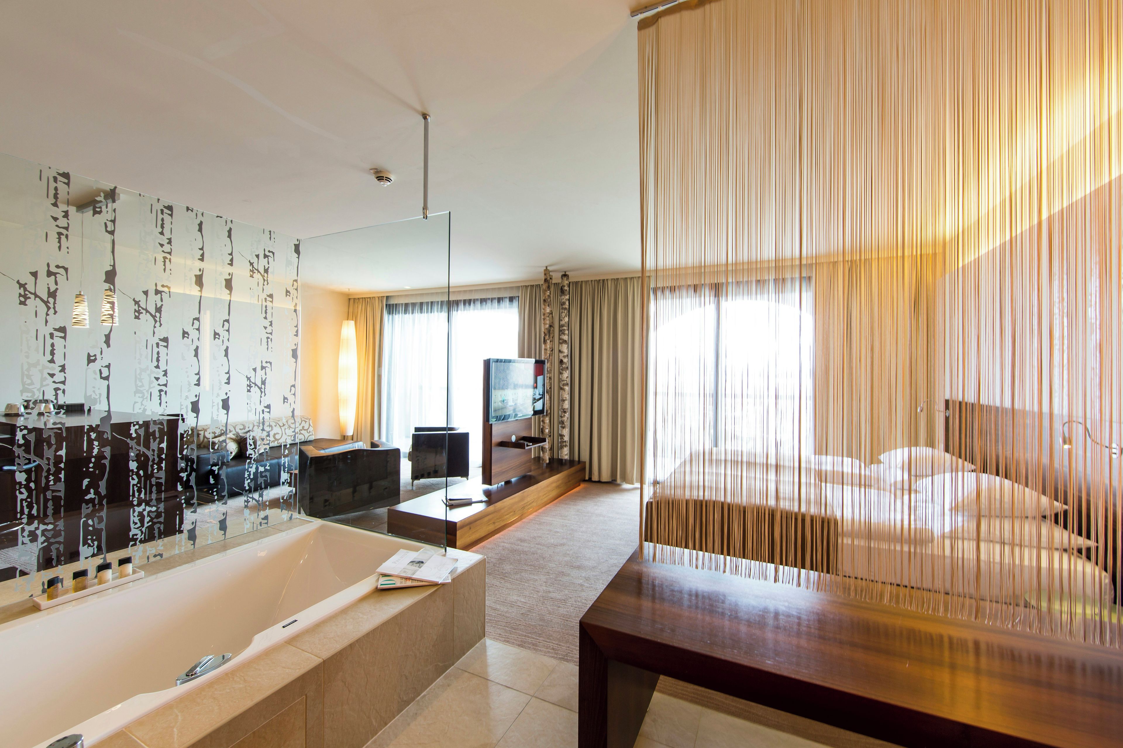 A hotel room with a large bathtub, a flat-screen TV, a sofa, and a dining table.