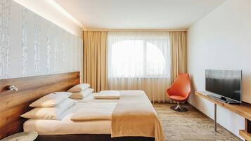 Habitación de hotel con cama, televisor, sillón y ventana con cortinas.