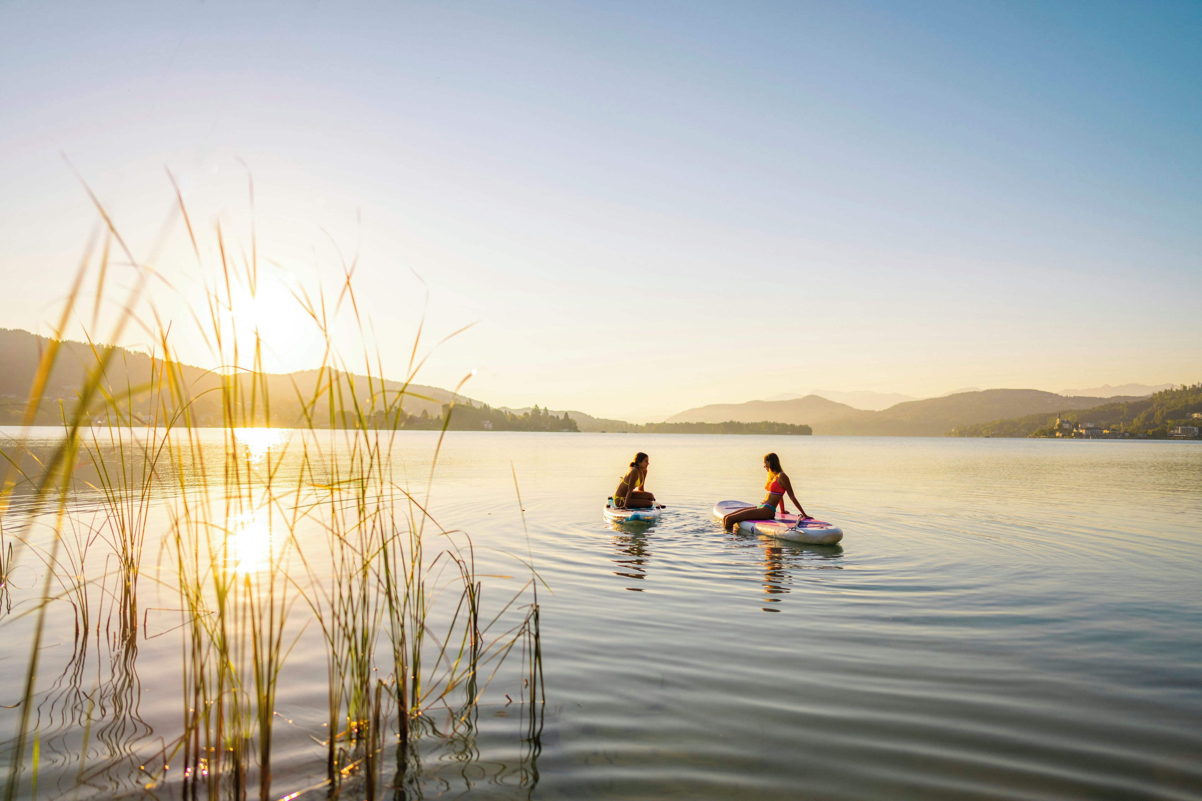 Two people on paddleboards on a calm lake with distant hills and a clear sky.