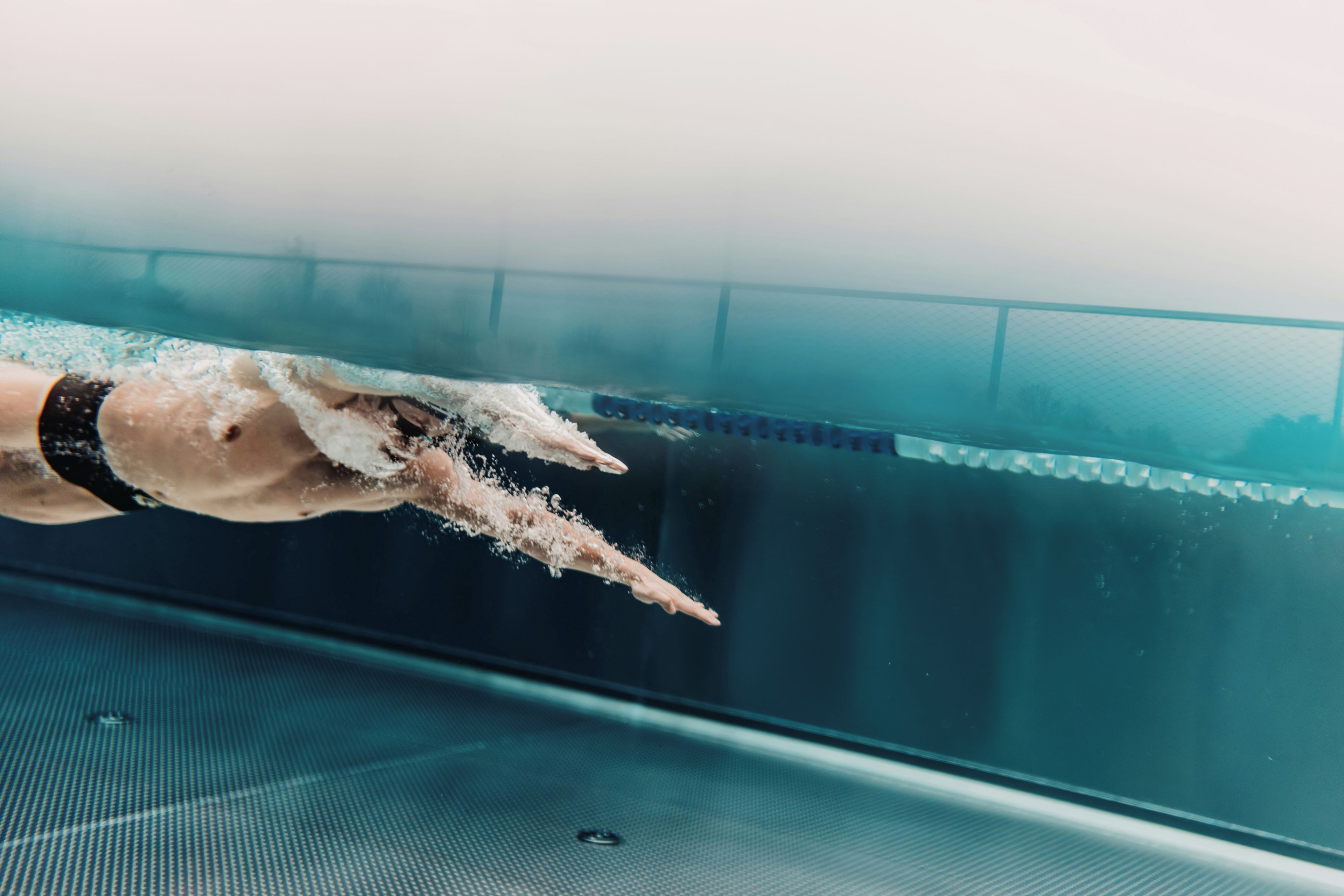 Brazo de nadador rompiendo la superficie del agua en una piscina.